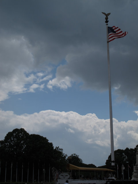 A flag waving defiantly in front of a cloudy sky.  And a duck (boat car) in the foreground.