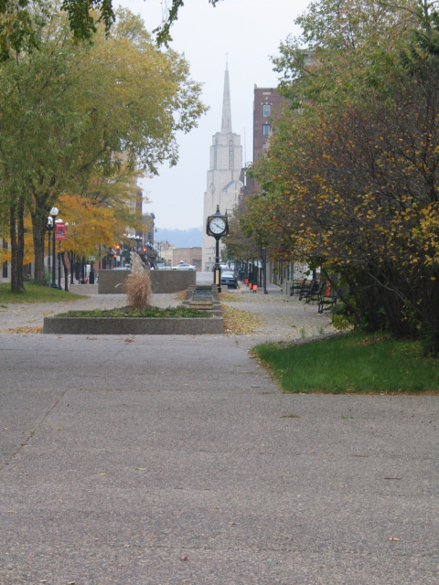 A public clock in LaCrosse, Wisconsin, surrounded by buildings and other stuff.