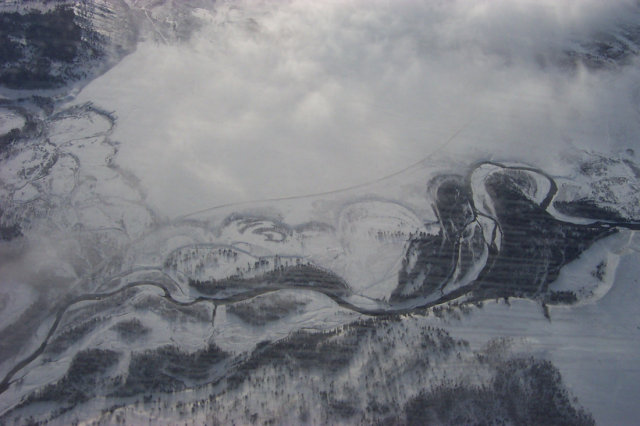 A river running through a snow covered valley, as seen from an airplane.