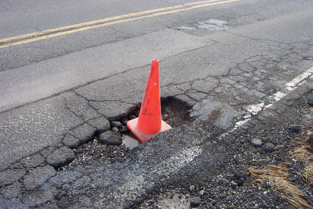 An orange cone sticking out of a pothole.
