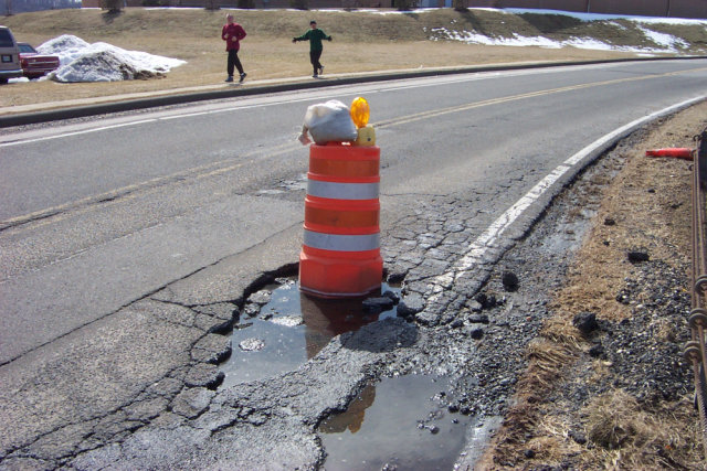 An orange barrel placed in a pothole large enough to fit it.