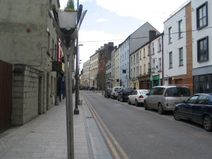 Parked cars and cramped houses line a street.